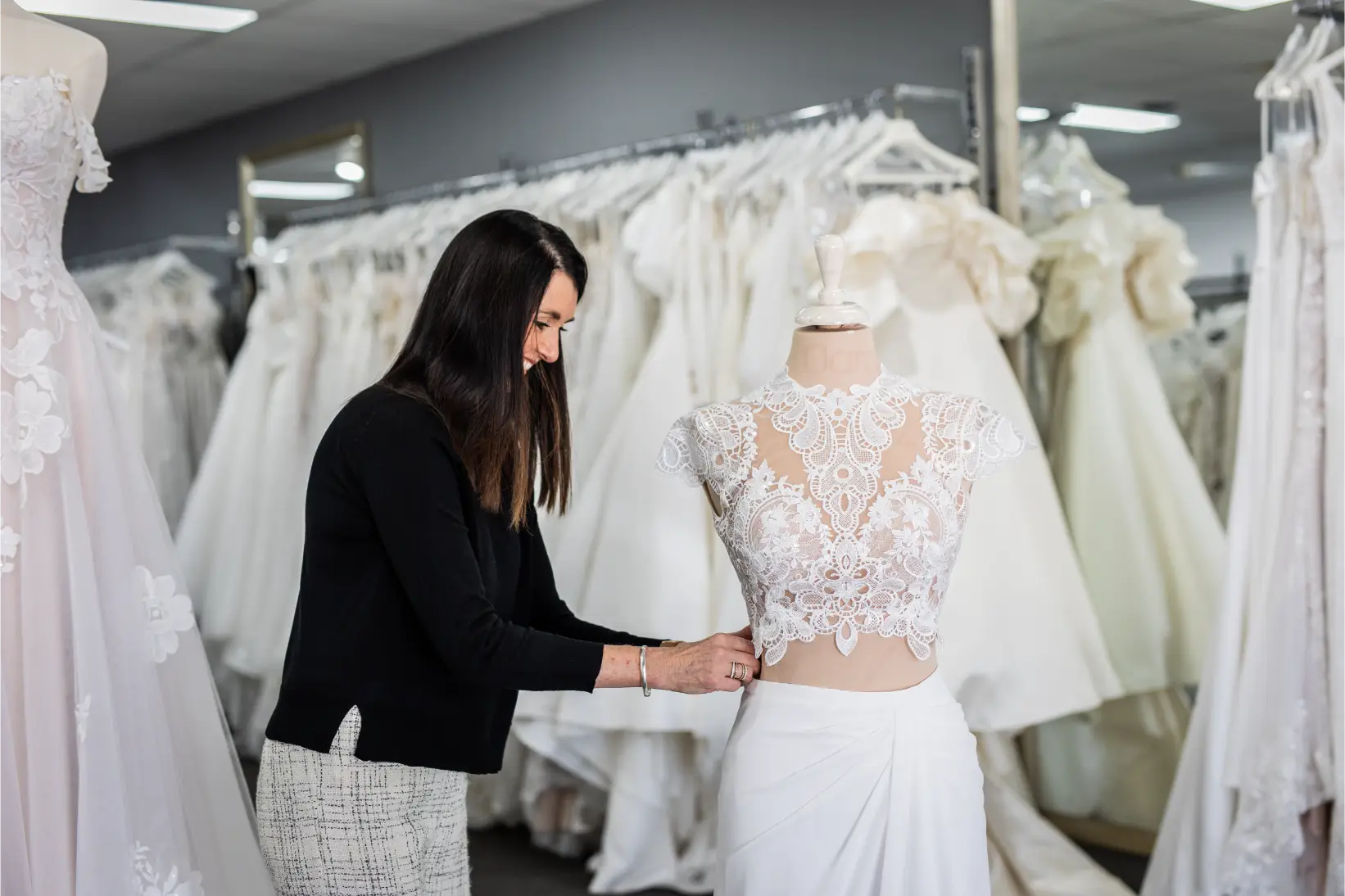 RSVP Bridal store owner showcasing a 2 piece wedding dress on a mannequin. Elegant wedding dresses hang on the rack in the background