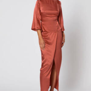 Model wearing the Cinta Dress by Winona Australia in copper – long sleeve satin gown with boat neckline, wrap skirt, and waist sash tie.