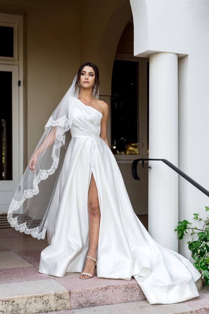 beautiful bride wearing a one shoulder wedding dress with a dreamtime designs veil. The Erica 2 tier veil in a soft tulle edge in a french chantilly lace