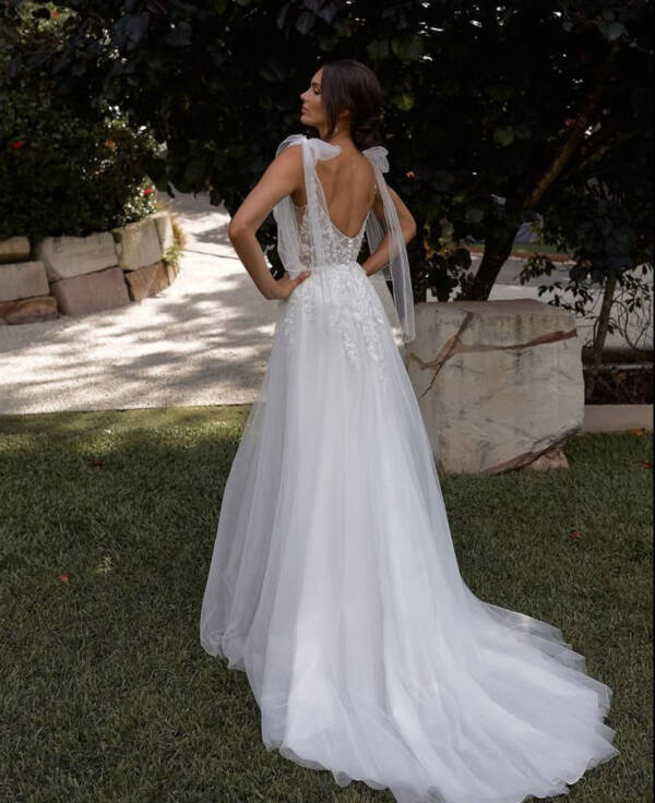 Ethereal beaded lace and tulle wedding dress in ivory with low V sheer back, tulle bows on shoulders, beaded lace applique cascading over waist. Soft tulle skirt flowing to a short train. Back view