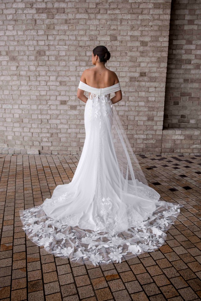 Back view of the Aria bridal gown showcasing the long, embroidered illusion train and off-the-shoulder detailing, with detachable tulle train flowing behind.