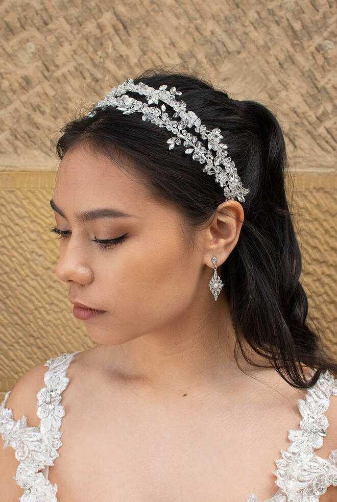 Bride wearing Cosima crystal twin band bridal headband with silver leaf-style crystals, styled with half-up hair and drop earrings.