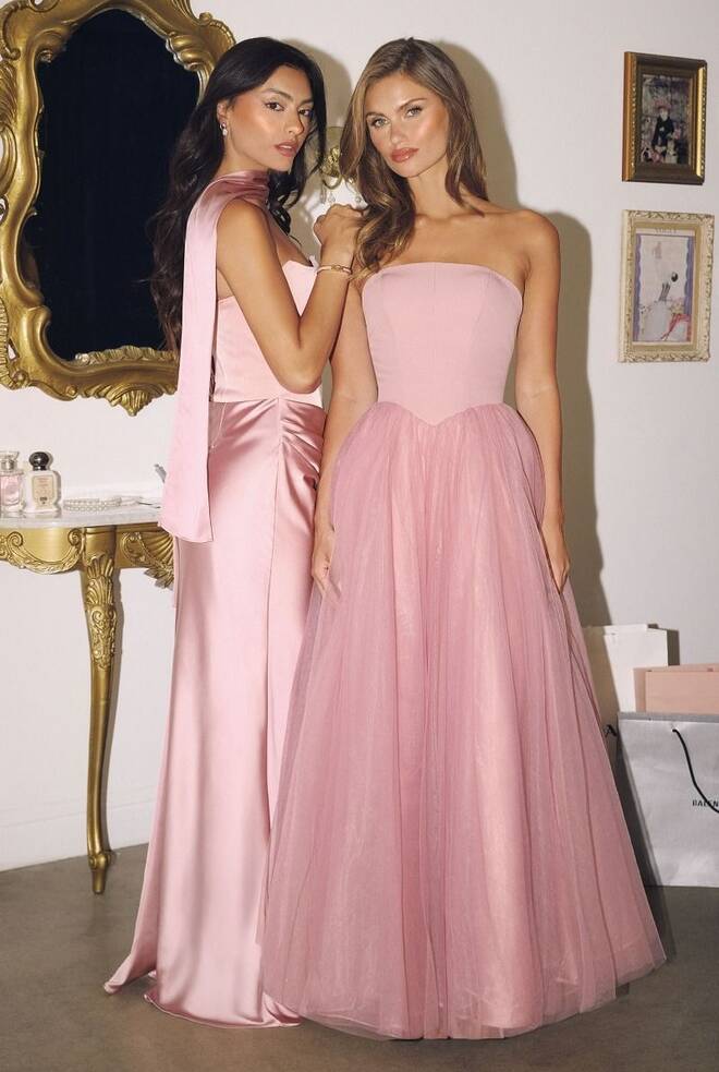 Two women in pink gowns; the right wears the Freya dress with a strapless crepe bodice, layered tulle A-line skirt, and oversized bow at the back.