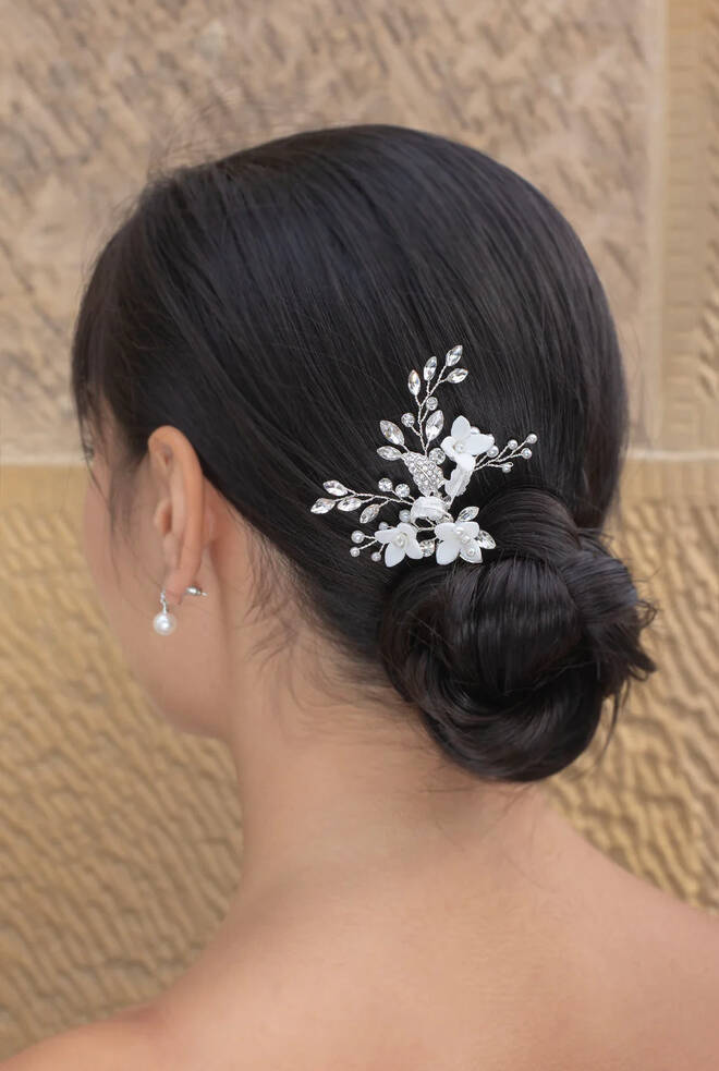 Woman with brunette hair wearing Lilith Hairpin WP132 in silver. Features white porcelain flower surrounded by sprigs of navette stone crystals.