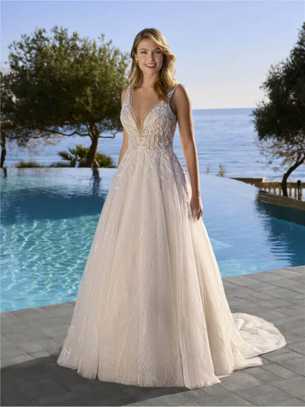 Bride wearing the Araluen Wedding Dress by Ladybird featuring a deep V-neck lace bodice and shimmering A-line tulle skirt with train, styled outdoors by a pool overlooking the ocean.