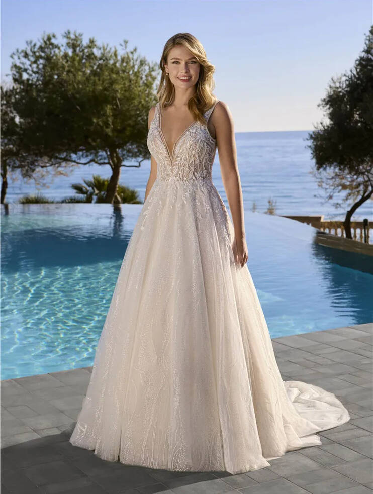 Bride wearing the Araluen Wedding Dress by Ladybird featuring a deep V-neck lace bodice and shimmering A-line tulle skirt with train, styled outdoors by a pool overlooking the ocean.