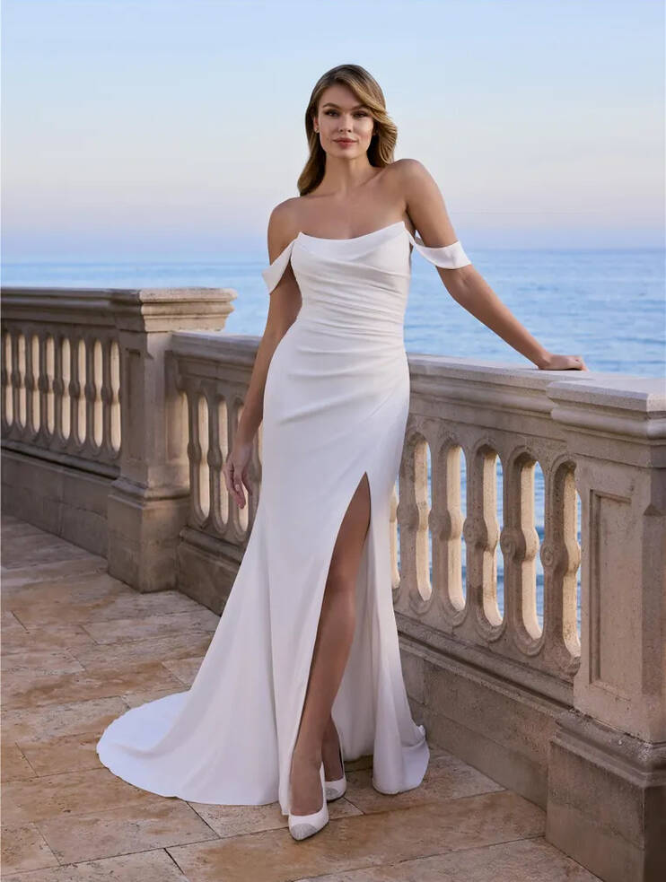 Aubrieta by Ladybird Bridal—off-the-shoulder crepe mermaid wedding dress with ruched bodice and thigh-high split, photographed on a seaside terrace