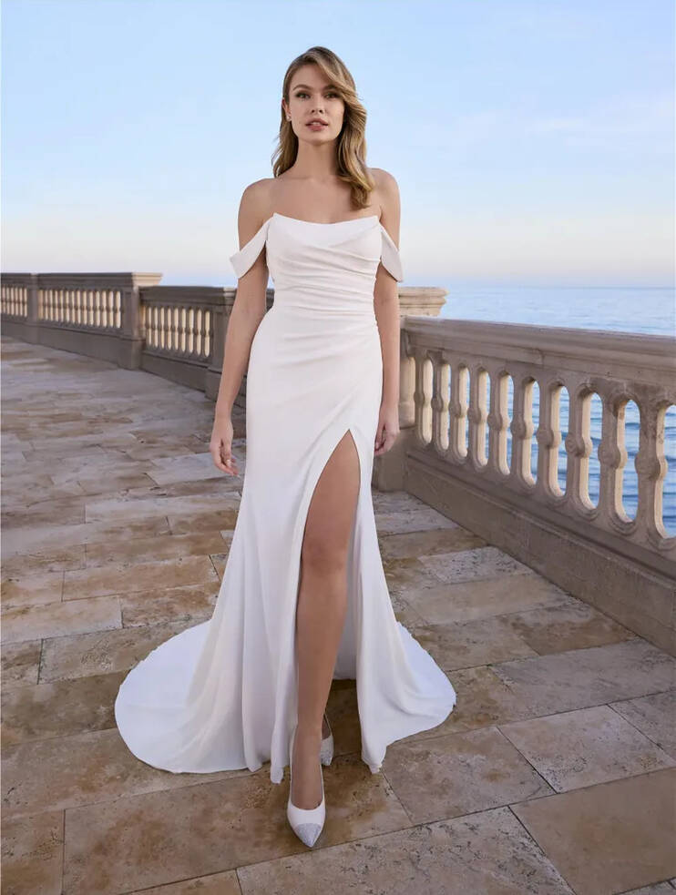 Aubrieta by Ladybird Bridal—off-the-shoulder crepe mermaid wedding dress with ruched bodice and thigh-high split, photographed on a seaside terrace