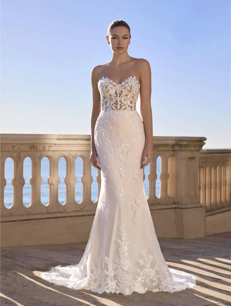 Bride wearing Ladybird mermaid wedding dress with sweetheart neckline, lace bodice, and tulle skirt against seaside backdrop.