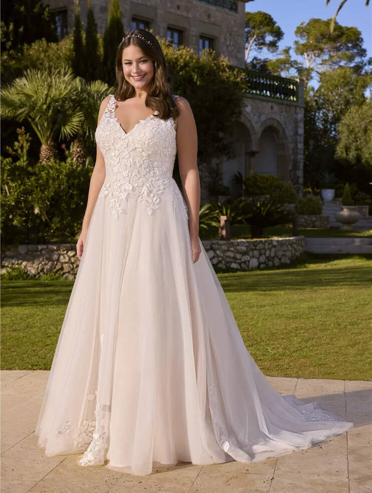 Bride wearing Ladybird princess V-neckline wedding dress with lace, tulle skirt, and beaded detail, standing in a garden setting.
