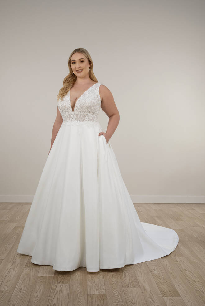 Bride wearing Stella York Style 7895 A-line wedding dress with deep V-neck lace bodice, satin skirt with pockets, and flowing train.