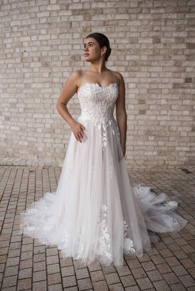 Bride wearing the Angelica gown from RSVP Bridal Collection, a strapless A-line wedding dress with floral lace appliqué and flowing tulle skirt.