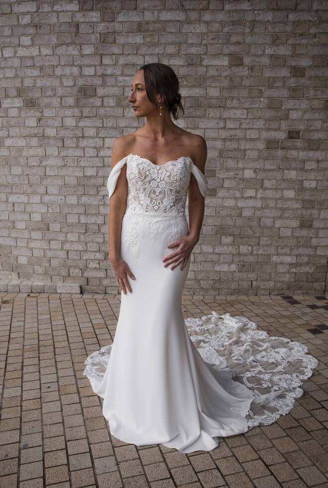 Bride wearing the RSVP Luna off-the-shoulder lace-bodice, crepe fit-and-flare wedding dress with scalloped cathedral lace train — front view.