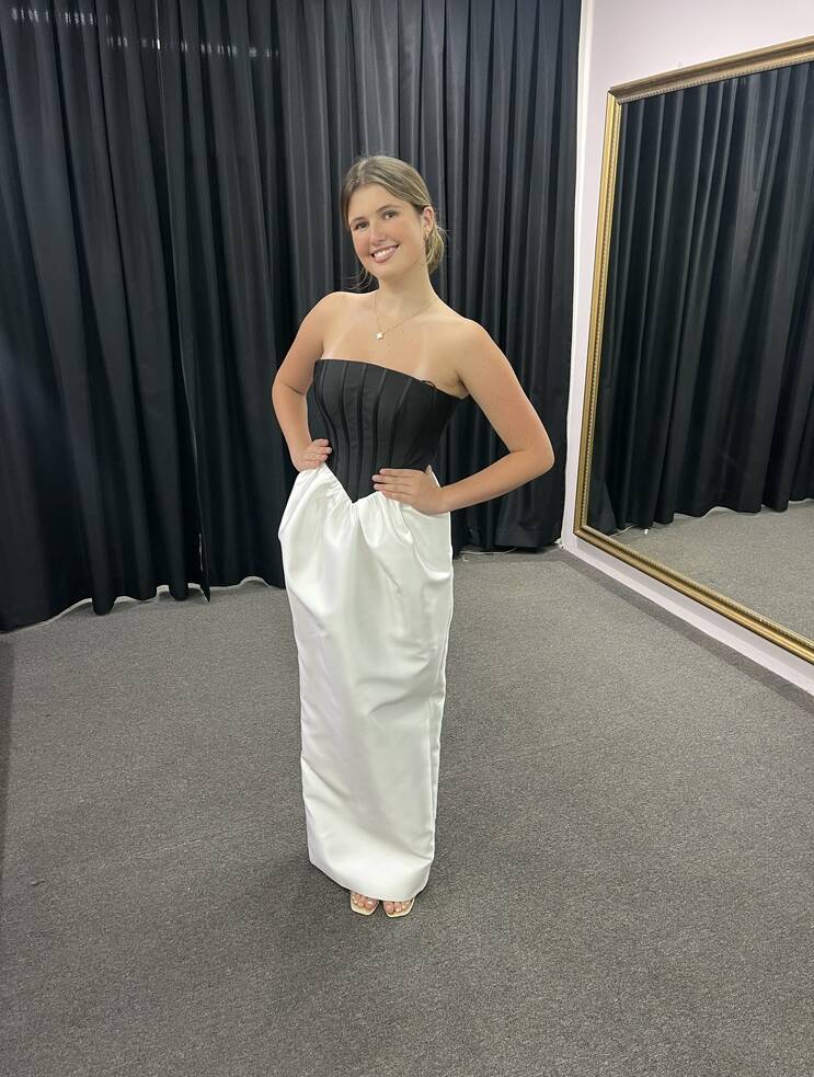Model wearing Bariano Rosemary strapless black corset with ivory satin-look column skirt, hands on waist, in fitting room.