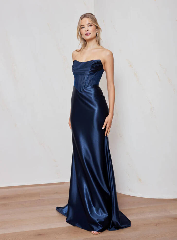 Model wearing navy metallic satin Coroa fitted floor-length formal gown by Tania Olsen, strapless scoop neckline with peaked bust cups and corset bodice.