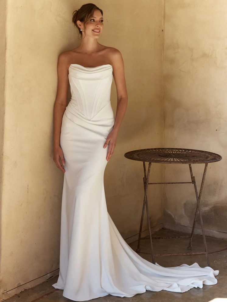 Model wearing the April wedding dress by Tania Olsen Bridal โ a strapless stretch crepe fit-and-flare gown with a straight neckline, pleated bust detail, basque waistline, and cathedral train.