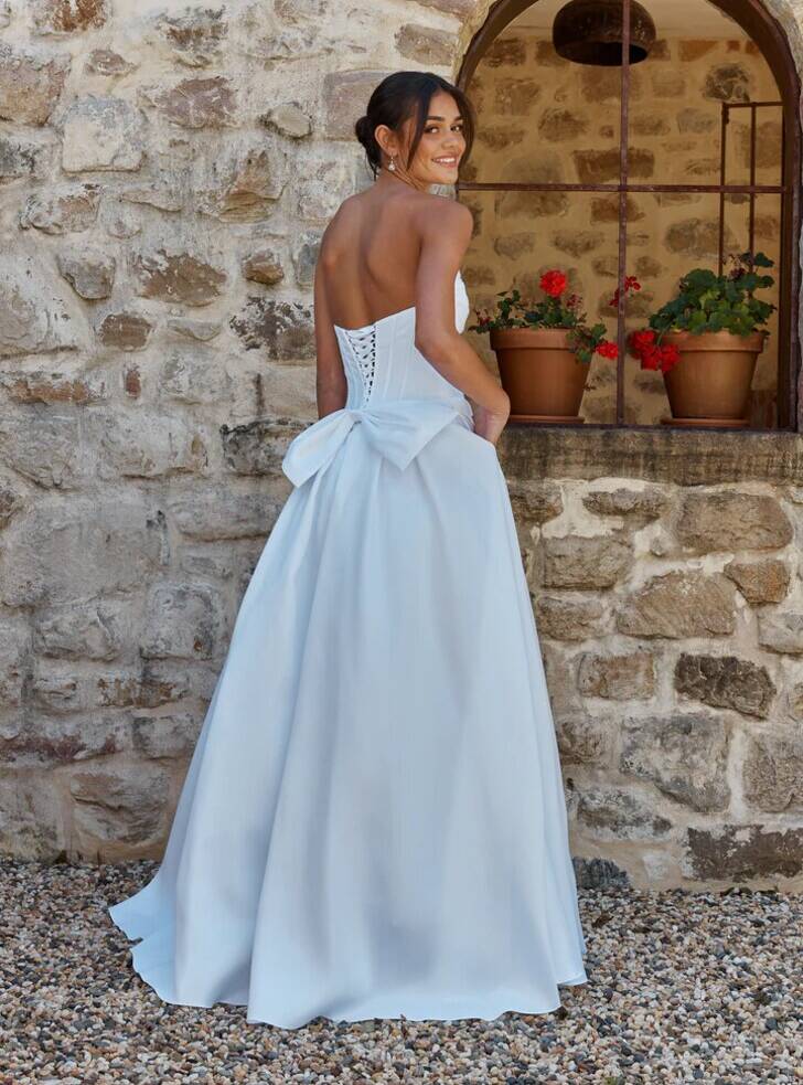 Back view of the Diora Debutante Dress by Tania Olsen Designs, in pure white satin featuring a lace-up corset back and oversized bow detail.