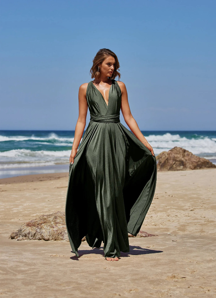 Model wearing the Tania Olsen PO31 multiway wrap dress in olive green with a plunging halter-style neckline and flowing floor-length skirt on a beach.