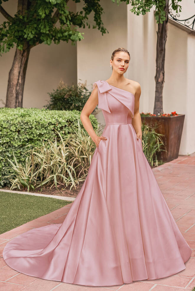 Cassandra by Jasmine Bridal blush pink one-shoulder A-line formal gown with statement bow detail, full skirt and hidden pockets.