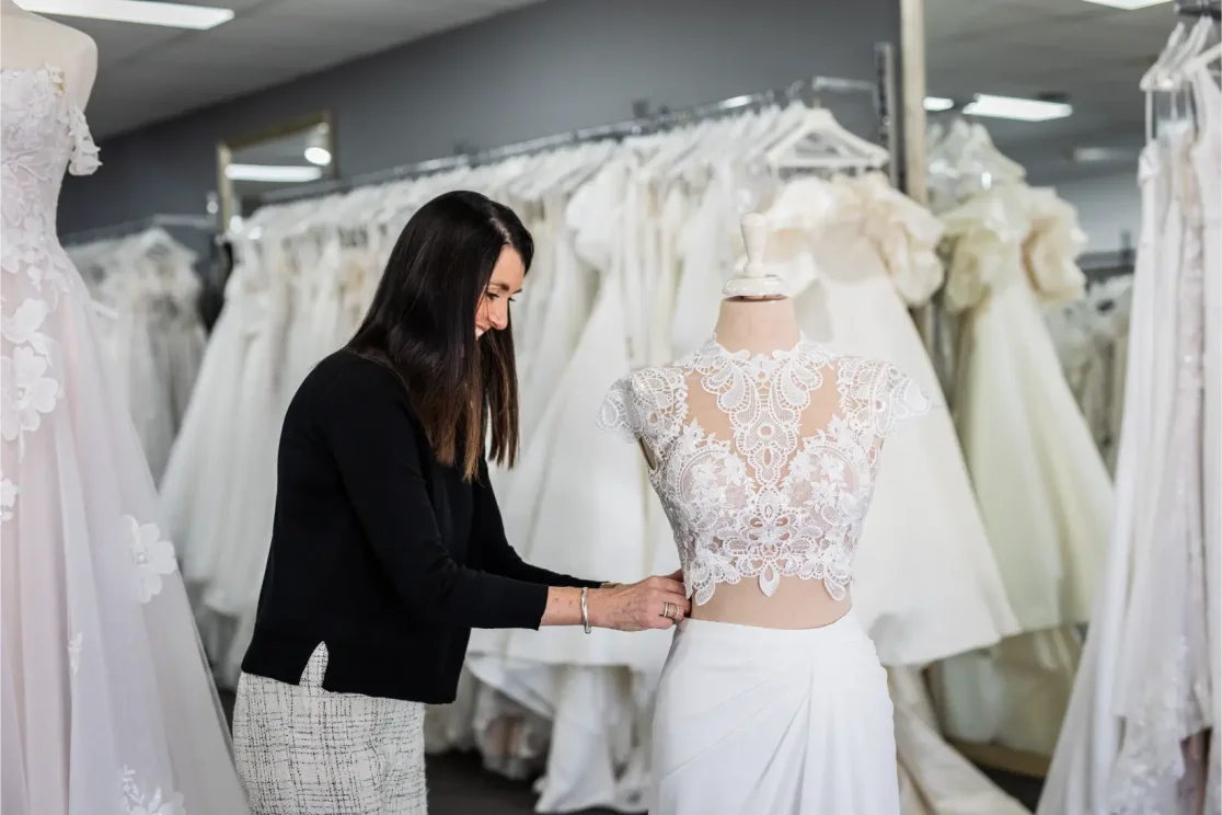 RSVP Bridal store owner showcasing a 2 piece wedding dress on a mannequin. Elegant wedding dresses hang on the rack in the background